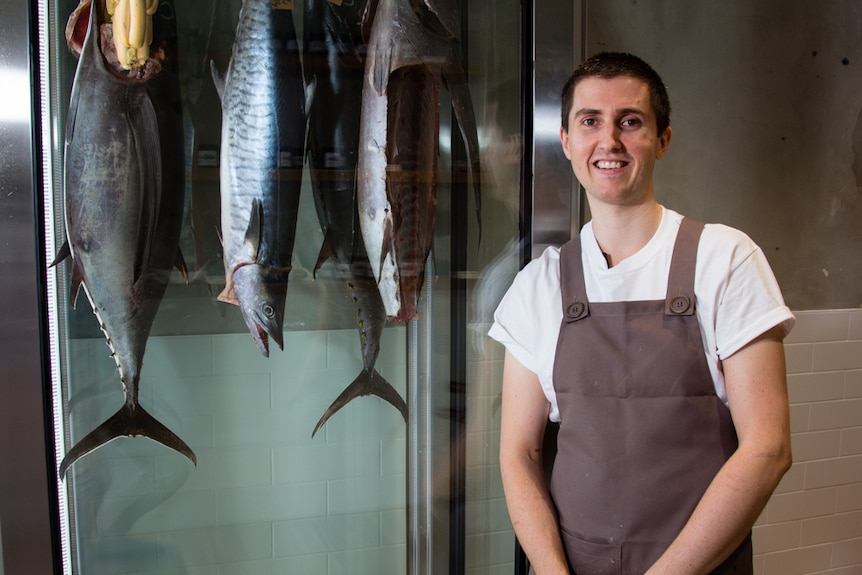 Joshua Niland standing in front of drying cabinet with several hanging fish displayed.