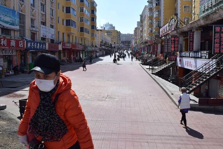 A resident wearing a face mask walks past a shopping street which used to be packed with people in Suifenhe city.