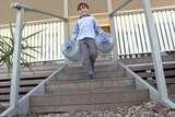 A child carries large water bottles down stairs