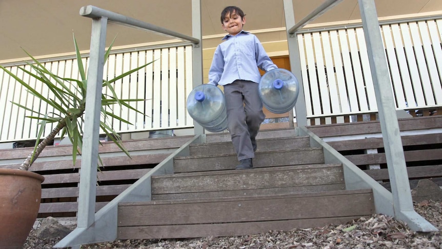 A child carries large water bottles down stairs