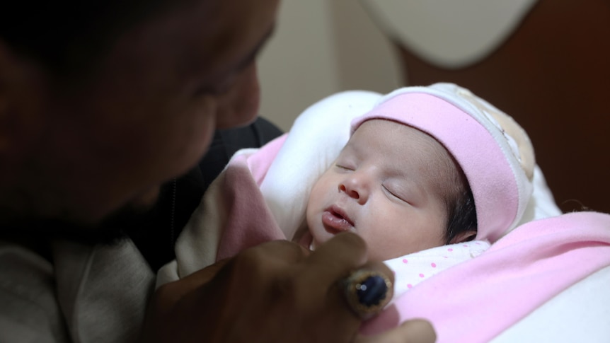 A person attends to a newborn wrapped in swaddling clothes