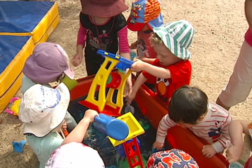 A group of children at a daycare pull toys out of a large red toy boxy.