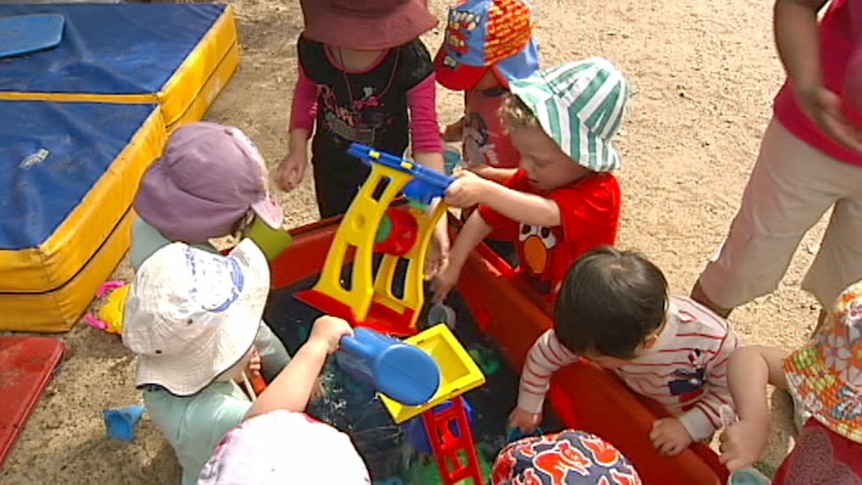 A group of children at a daycare pull toys out of a large red toy boxy.