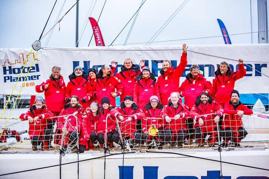 Happy crew including Phillip Hulcome, dressed in red wet weather gear on board their yacht at anchor in Seattle.