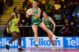 An Australian Diamonds goal keeper catches the ball while off the ground, as a Jamaican goal shooter looks dejected behind her.