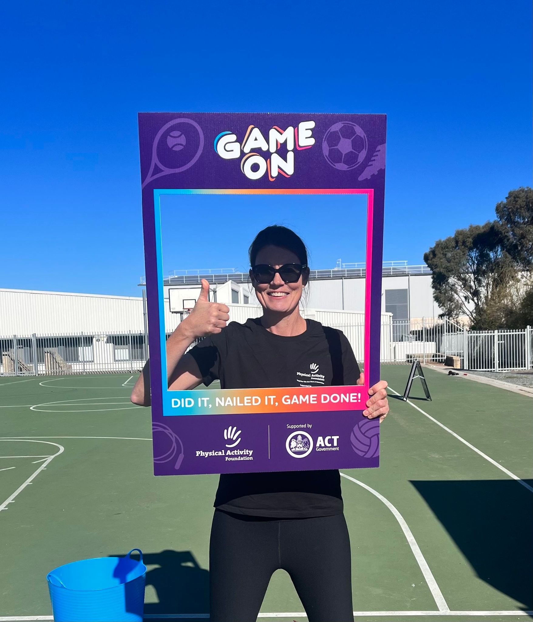 A woman giving a thumbs up in the middle of a cardboard sign that is cut out like a frame. 