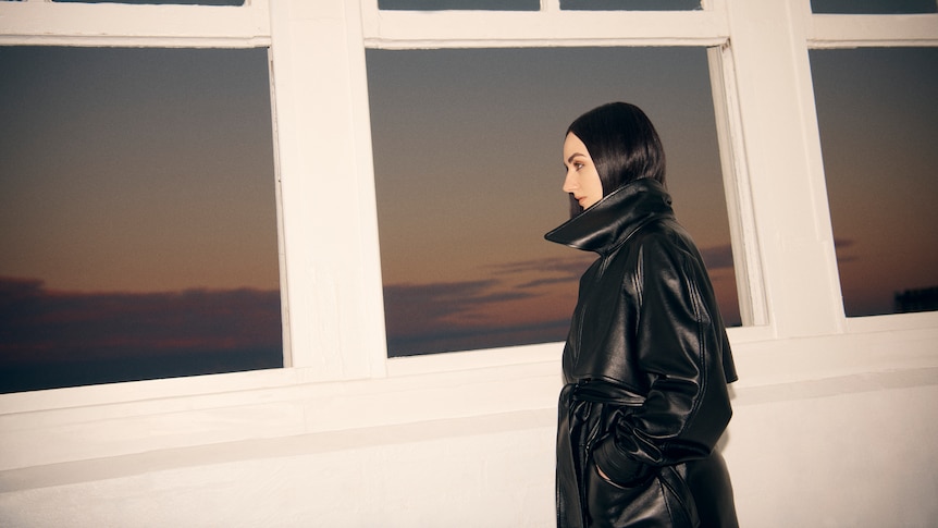 Meg Mac in profile against a window frame against a dusk skyline