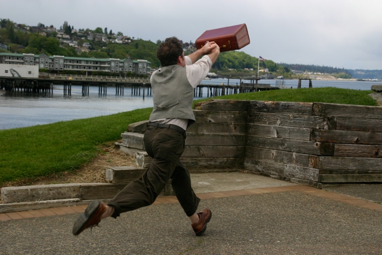 A performer in full stretch holding a suitcase.