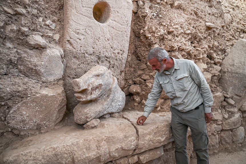 Necmi observes a stone carving of a wild boar's head.