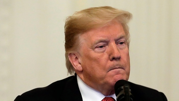 Donald Trump wearing a black suit jacket, white shirt and red and black tie purses his lips as he speaks into a microphone