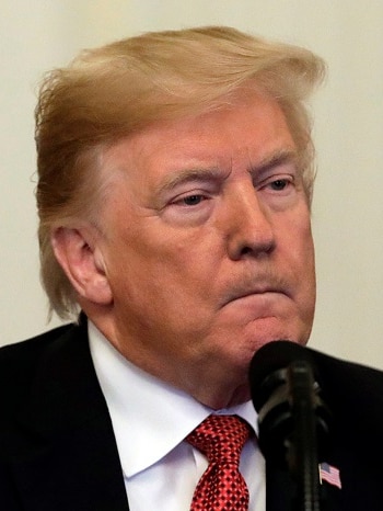 Donald Trump wearing a black suit jacket, white shirt and red and black tie purses his lips as he speaks into a microphone