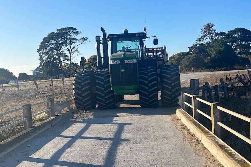 A large tractor in front of a narrow bridge.
