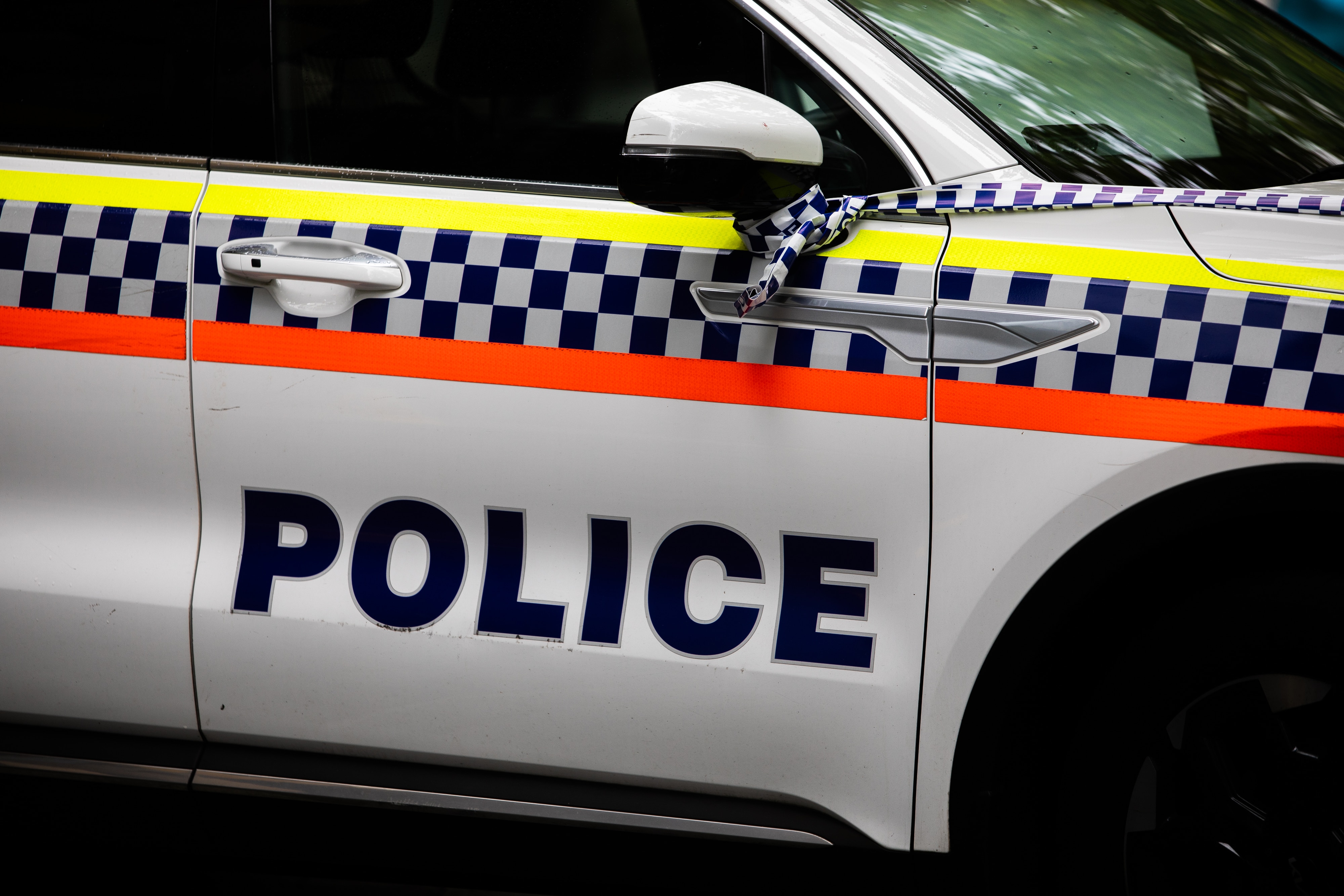 A door of a police car with police tape tied to the side mirror.
