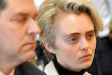 A woman with short blonde hair appears in court sitting next to a man who may be her lawyer.