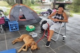 A homeless woman sitting in a camp chair with a tent and pile of clothes behind her