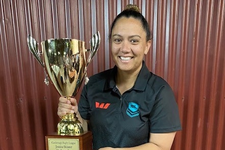 A woman stands proudly holding a new trophy cup