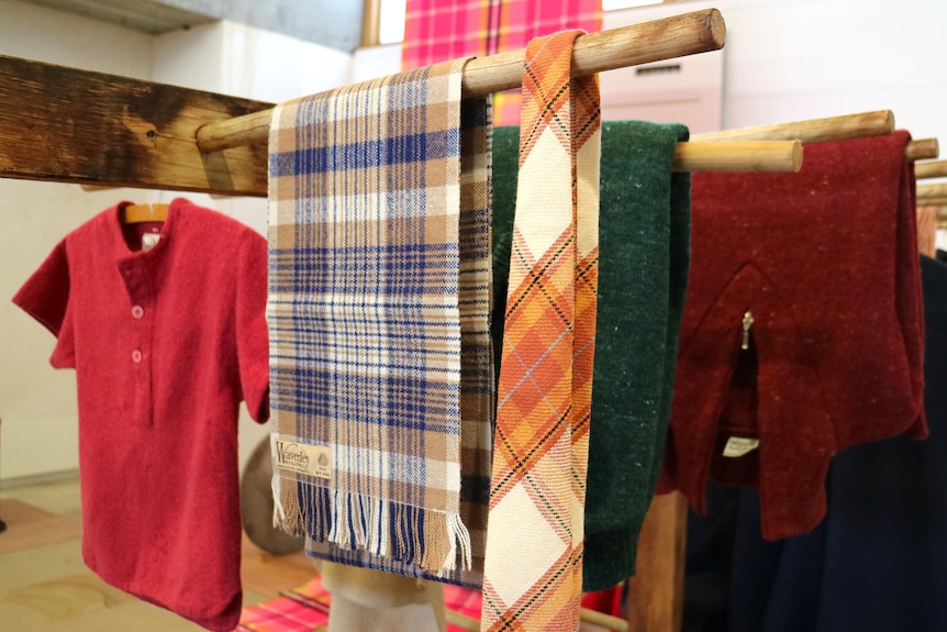 a woollen shirt, tie and blanket hang on timber rods