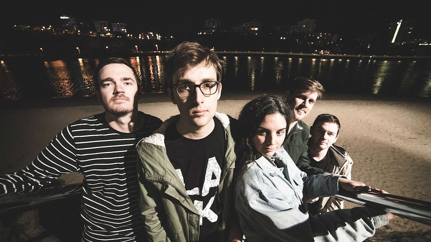 The band standing on a staircase with a river in the background at night