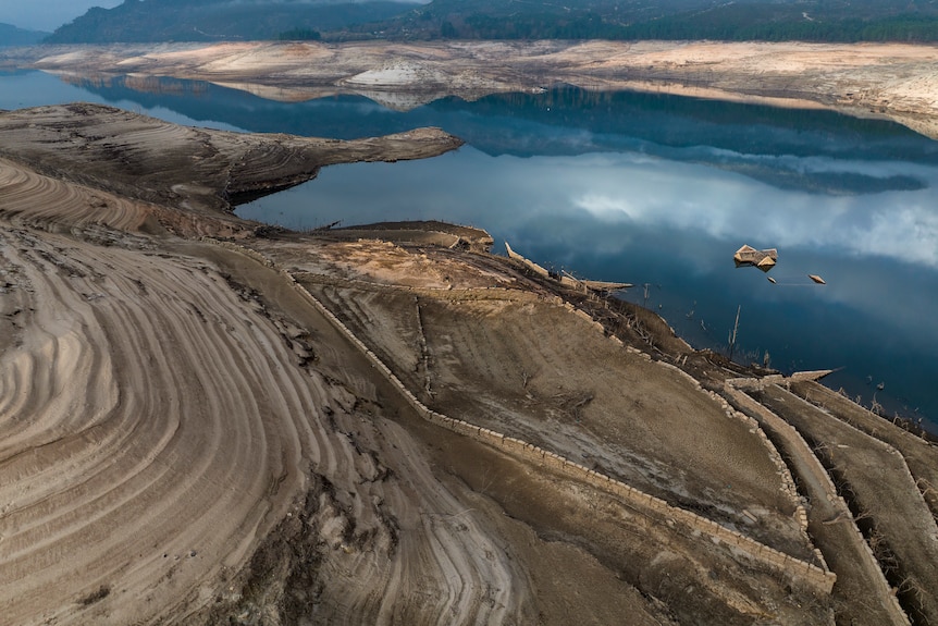 An aerial shot of the Lindoso reservoir with a roof floating in the middle of the water.