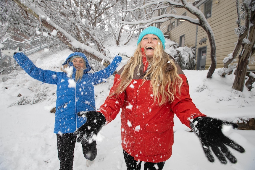 zwei Frauen werfen mit einem Lächeln im Gesicht Schnee in die Luft