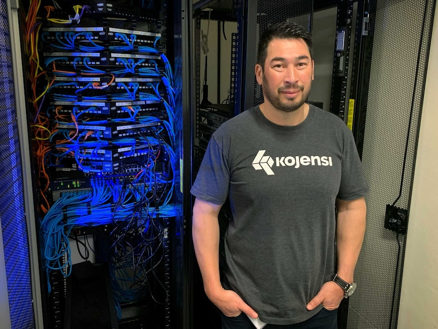 archTIS CEO Daniel Lai stands in front of a cabinet of protruding cables