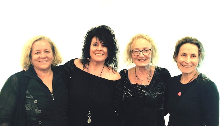 four middle aged women standing side by side looking happy and smiling