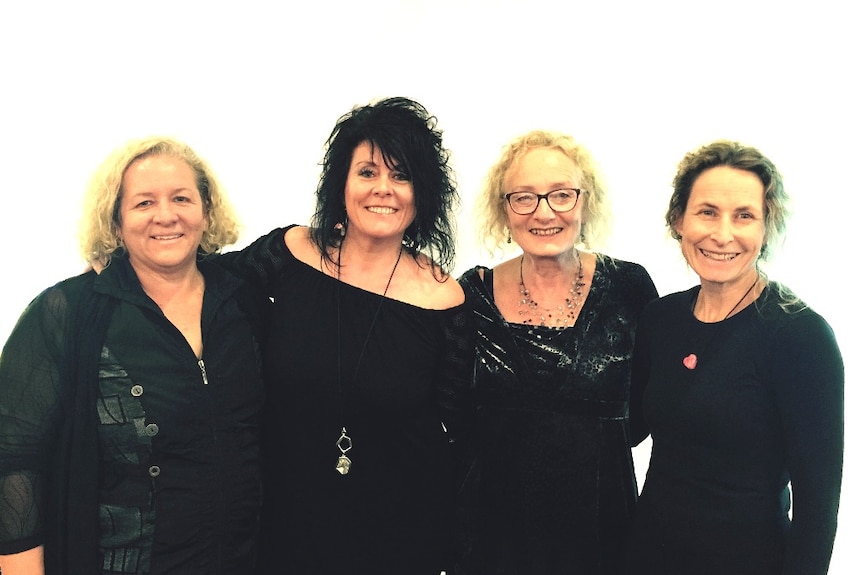 four middle aged women standing side by side looking happy and smiling