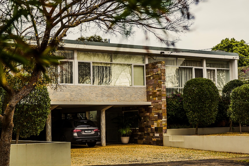 A shot of a mid-century style home with a car parked in the driveway.