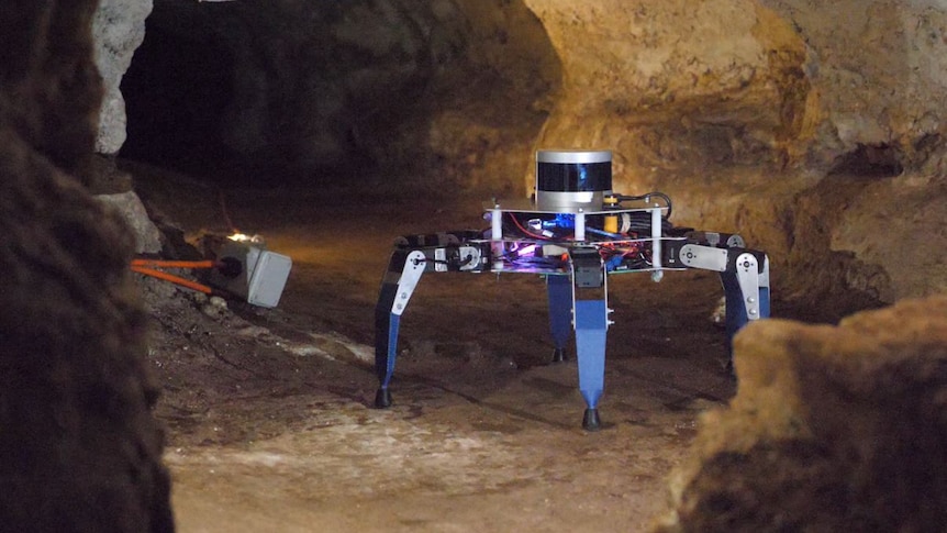 The spider like robot is standing in a small but well-lit cave passageway 