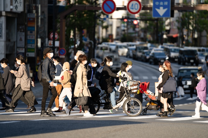 A group of people walk on a crosswalk with their bikes and wearing masks.