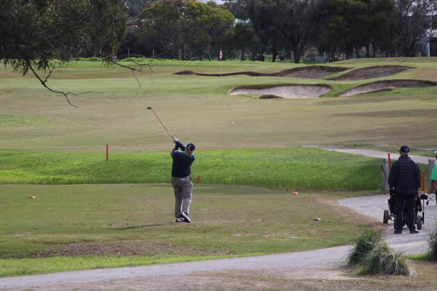 Un golfeur joue un coup sur un terrain de golf, avec des bunkers visibles au loin