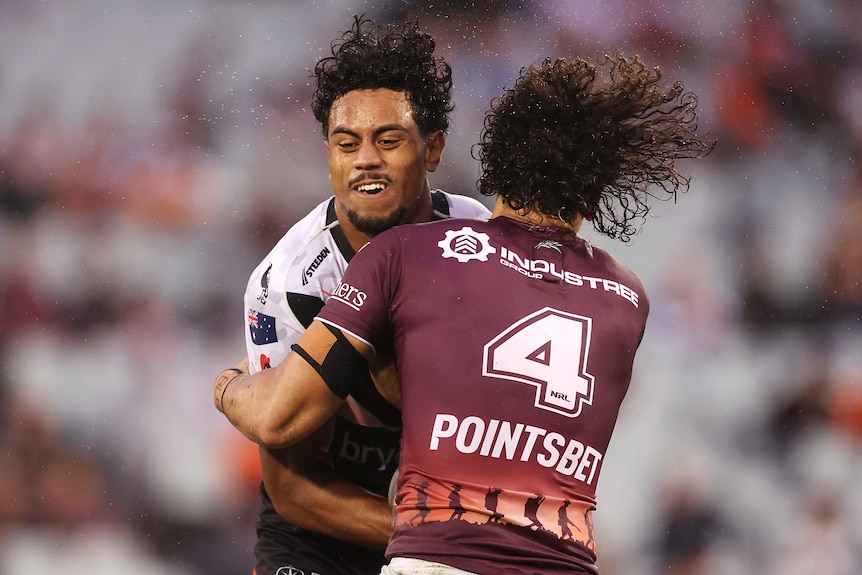 A Wests Tigers NRL player is tackled by a Manly opponent.