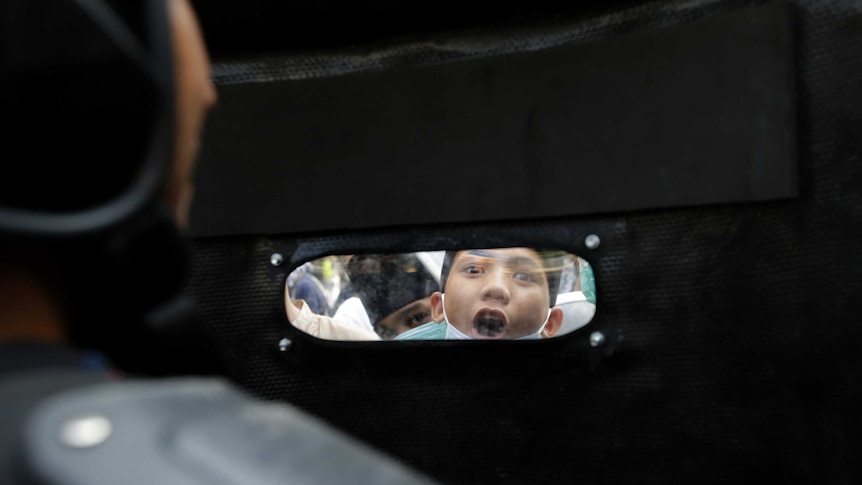 A protester is seen through the window of an Indonesian police officer's riot shield in Jakarta.