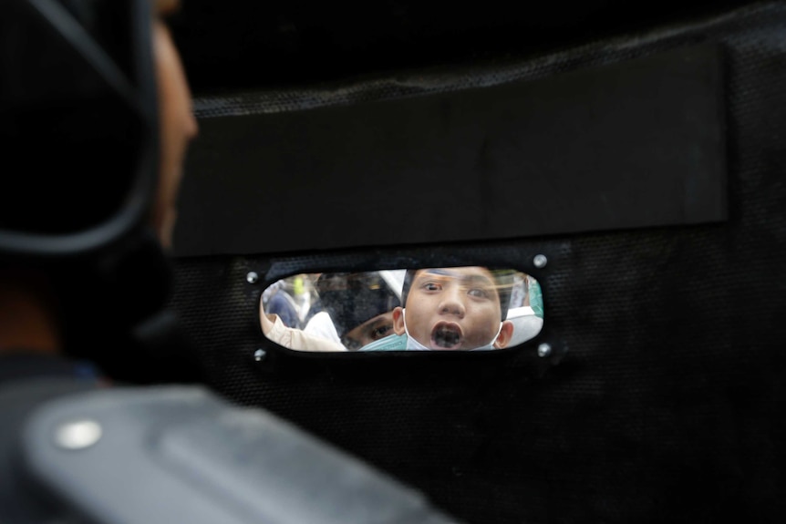 A protester is seen through the window of an Indonesian police officer's riot shield in Jakarta.