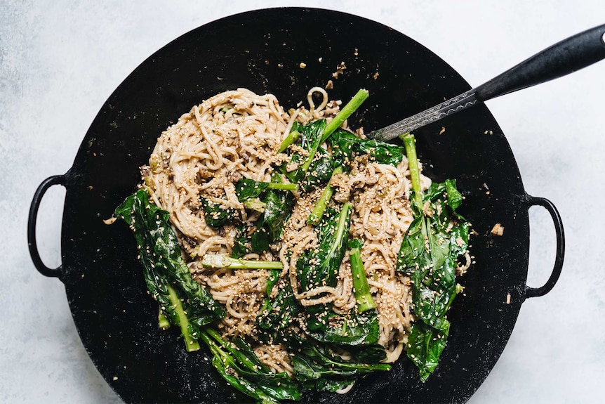 A wok full of  noodles with a creamy  sauce and topped with Asian greens, sesame seeds and mushroom for Chinese New Year.