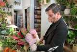 Shane Sipolis, wearing a black jacket and a patterned face mask, holds a bunch of flowers.