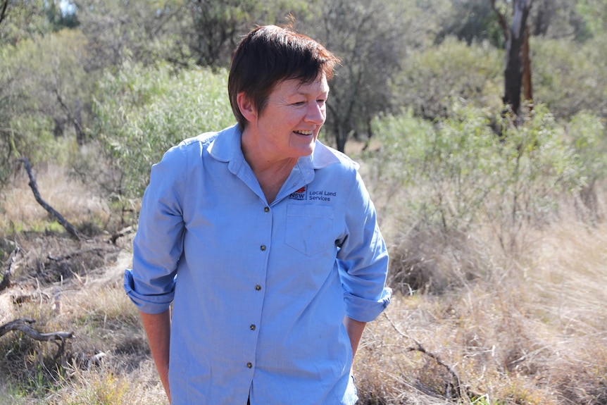 A woman with dark, short hair, wearing a work shirt and standing in bushland.