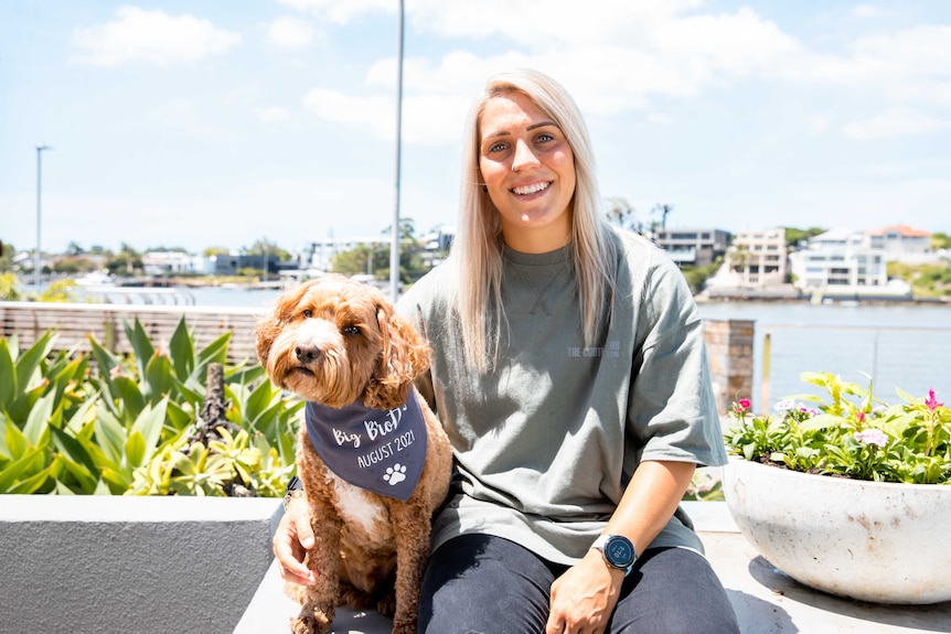 A woman and a dog sit on a back deck in front of a waterway.