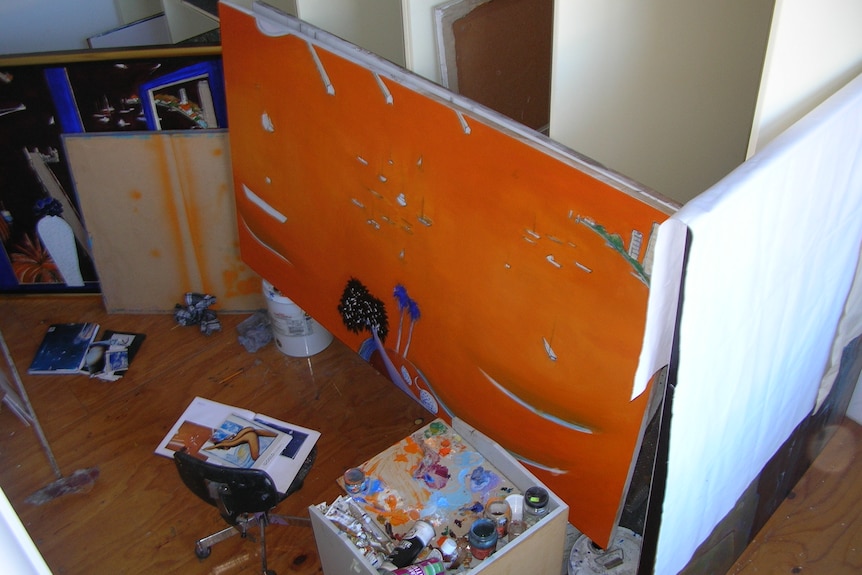 A photo shot from high of a large orange painting in progress with art supplies in front of it 