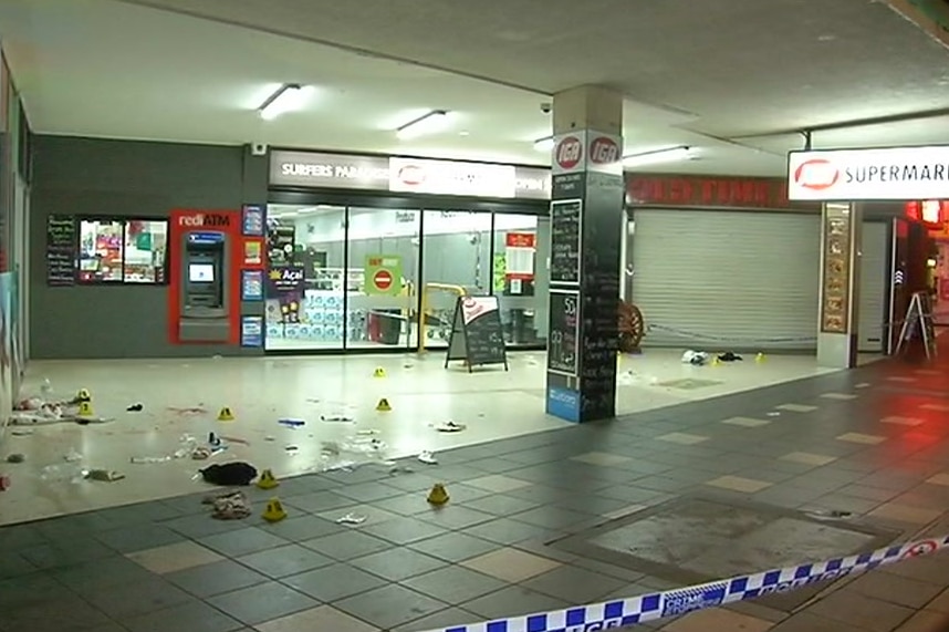Crime scene markers, rubbish and blood can be seen outside an IGA supermarket. There is police tape around the scene.
