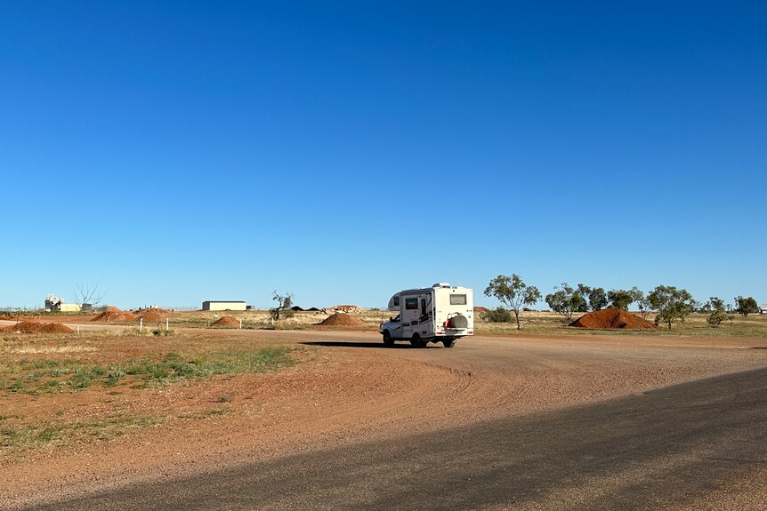 Campervan driving on an outback round, mounds of gravel on either side. 