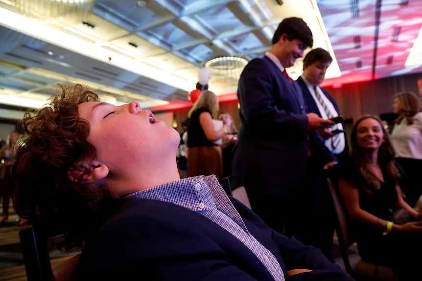 A boy sleeps with his mouth open in a ballroom