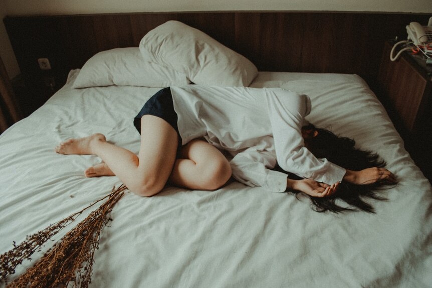 A woman is curled up on a bed holding her stomach 