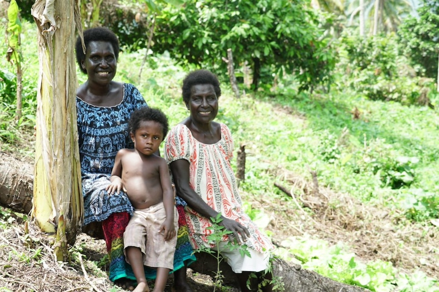 Susan sits with her child and neighbour on a fallen tree in the garden.