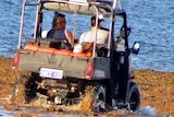 Two men sit in an amphibious vehicle driving to the water.