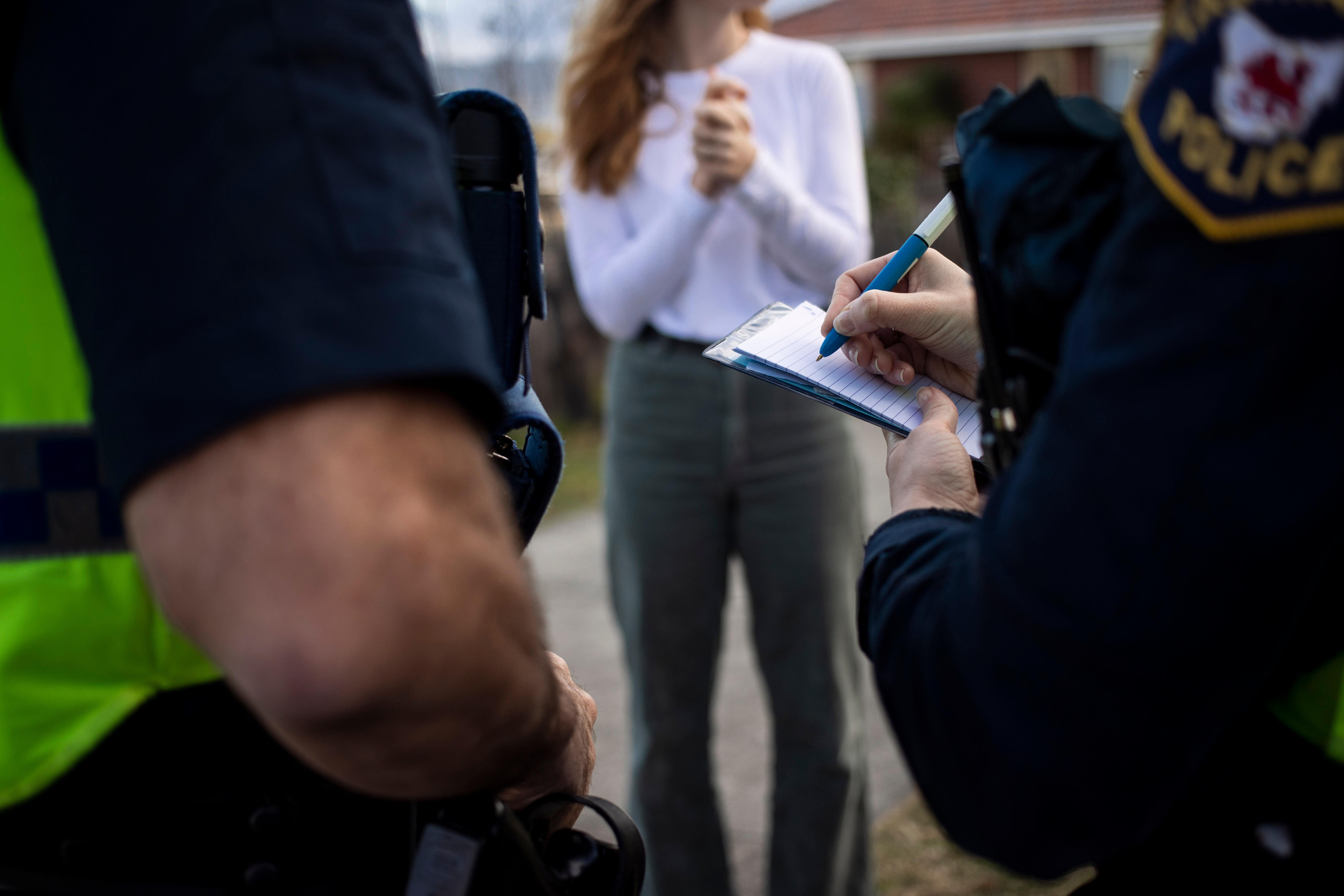 Two police officers take notes while talking to an unidentified woman.