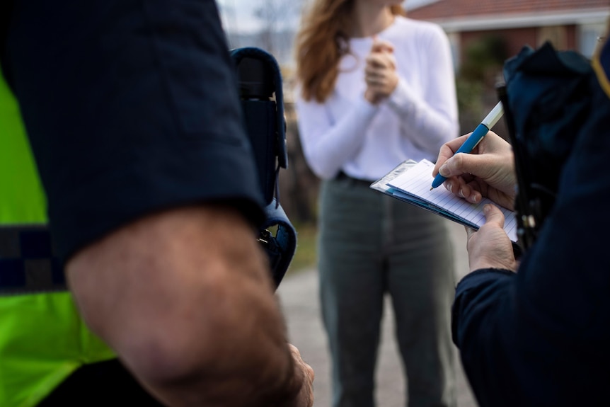 Two police officers take notes while talking to an unidentified woman.