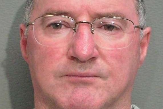 Headshot of wanted fugitive, Graham Potter with short grey hair and wearing glasses.
