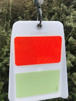 A white plastic tag with a red reflective patch for handing on powerlines
