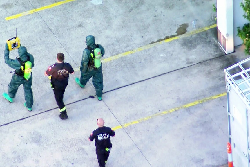 two men dressed in hazmat protective clothing walk with fire personnel outside a building